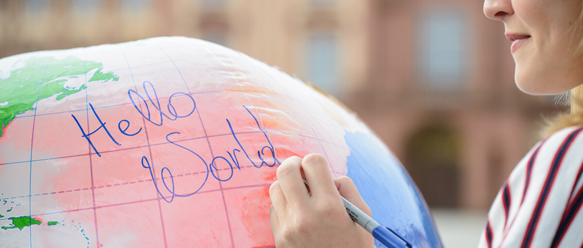 Eine Frau schreibt mit einem Stift auf eine Weltkugel "Hello World".