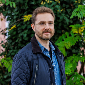 Prof. Dr. Ivan Balykin in blauer Jacke vor grünen Pflanzen.