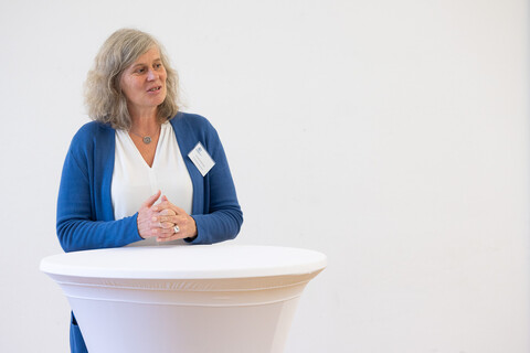 Eine Person trägt eine weiße Bluse sowie einen blauen Cardigan und steht an einem Stehtisch. Die Person heißt Ursula Schlichter.