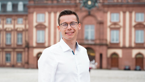 Louis Vandepoele. He is wearing a white shirt and is standing in front of the castle on the Ehrenhof.