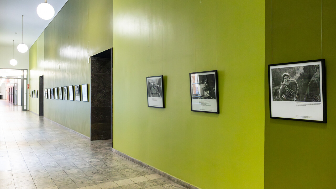 Viele Schwarz-Weiß-Fotografien von Personen hängen in einem grünen Flur.