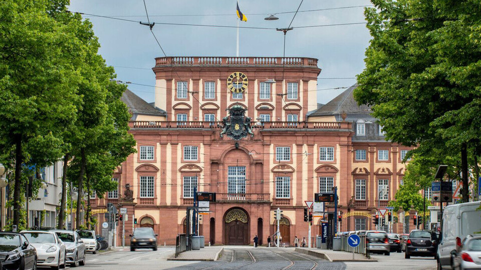 Blick aus den Quadraten entlang der Straßenbahnschienen und der Haltestelle Schloss auf den Mittelbau des Barockschlosses Mannheim.