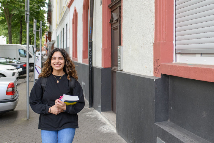 Lachende Studentin mit Buch in der Hand läuft durch eine Straße in Mannheim