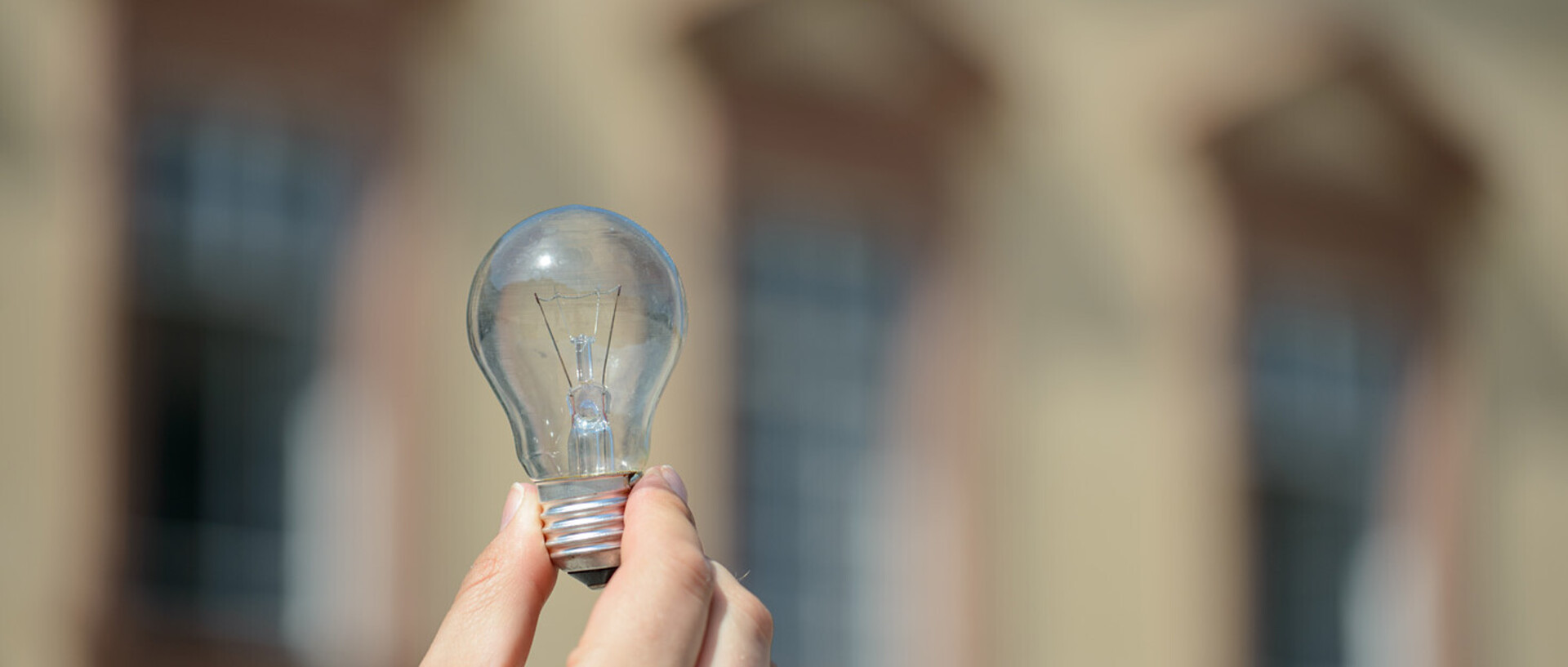 Eine Hand hält eine Glühbirne vor dem Mannheimer Schloss hoch.