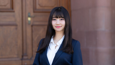Kyung Eun Park. She is wearing a blue jacket over a white shirt and is standing in front of one of the castle doors.