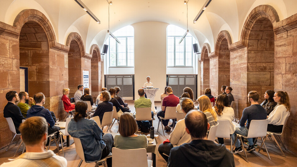 Viele Menschen sitzen auf Stühlen in den Katakomben der Uni Mannheim und hörem einem Vortrag zu.
