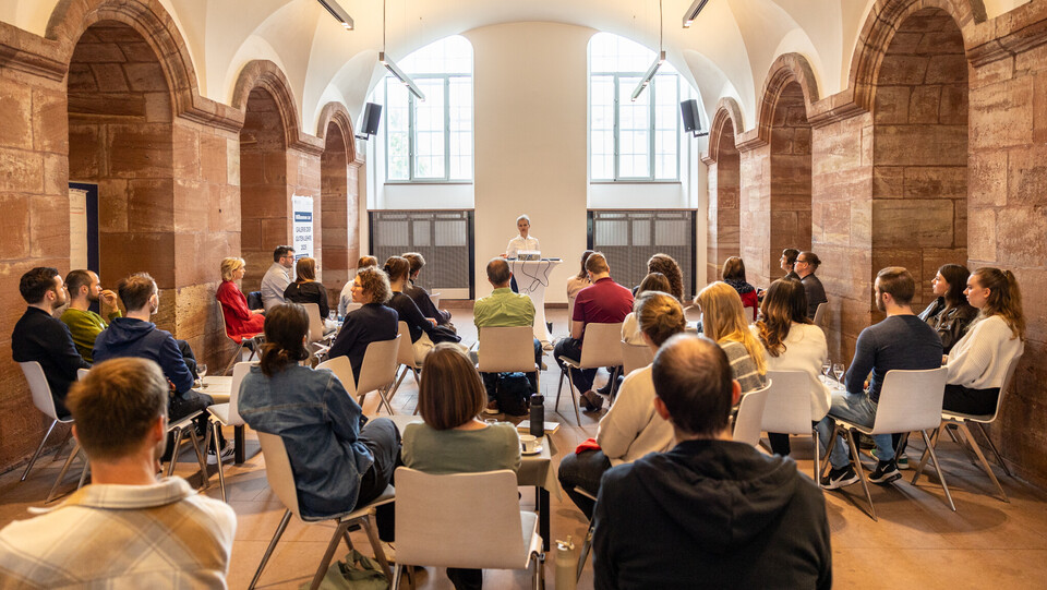 Viele Menschen sitzen auf Stühlen in den Katakomben der Uni Mannheim und hörem einem Vortrag zu.