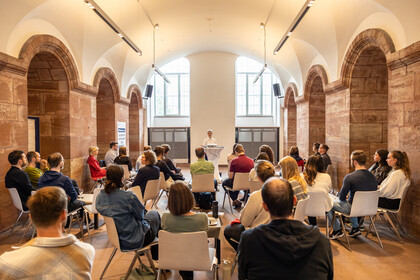 Viele Menschen sitzen auf Stühlen in den Katakomben der Uni Mannheim und hörem einem Vortrag zu.
