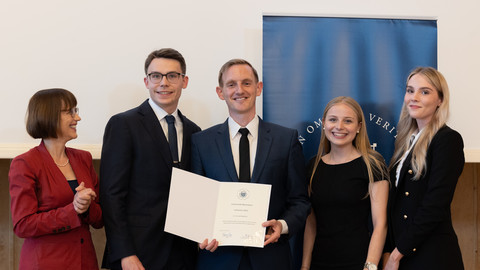 Fünf Personen in schicker Kleidung stehen nebeneinander. Die Person in der Mitte hält eine Urkunde für den Lehrpreis der Uni Mannheim an Conrad Waldkirch in der Hand.
