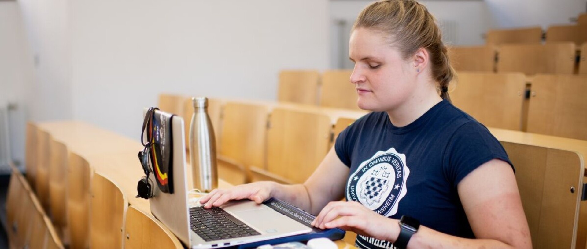 Eine Studentin mit Sehbehinderung sitzt in einem Vorlesungssal an ihrem Laptop mit Braillezeile