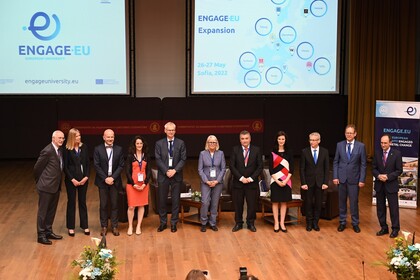 Elf Personen in schicker Kleidung stehen nebeneinander. Im Hintergrund wird das Logo von Engage.EU an die Wand projiziert. 