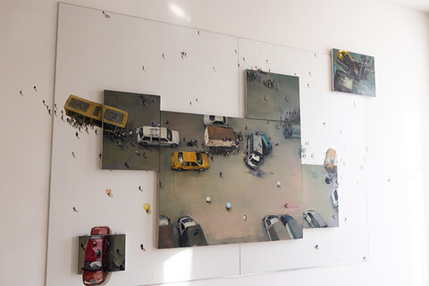 Gemälde einer Person mit Miniaturfiguren, das sich auf die Wand fortsetzt. An einer Stelle sind Autos, Figuren und ein Verkehrschaos mit Unfall dargestellt