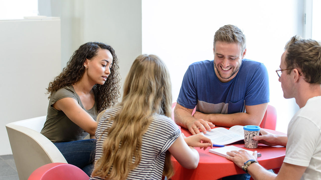 Vier Studierende sitzen an einem roten, runden Tisch und lernen gemeinsam.