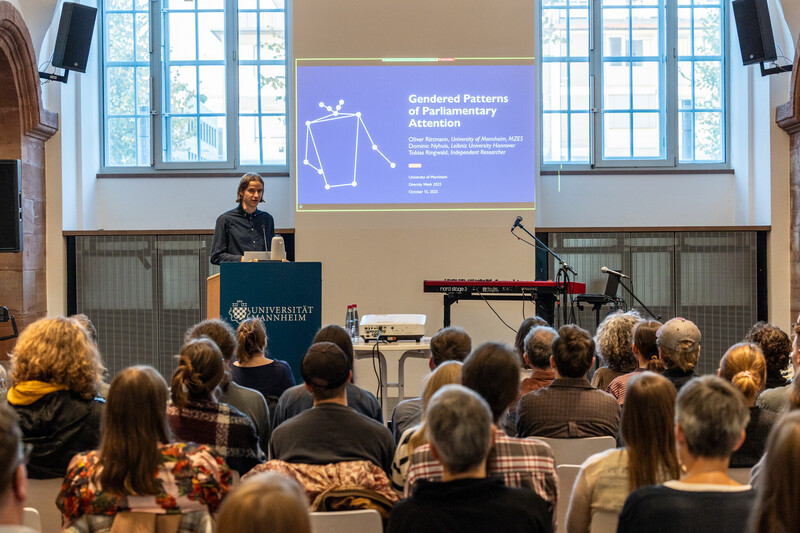 Zuschauer in den Katakomben zur Diversity Week hören dem Vortrag von Dr. Oliver Rittmann zu. Dr. Rittmann steht am Pult, die Powerpoint Folie ist im Hintergrund zu erkennen und zeigt das Deckblatt des Vortrags.