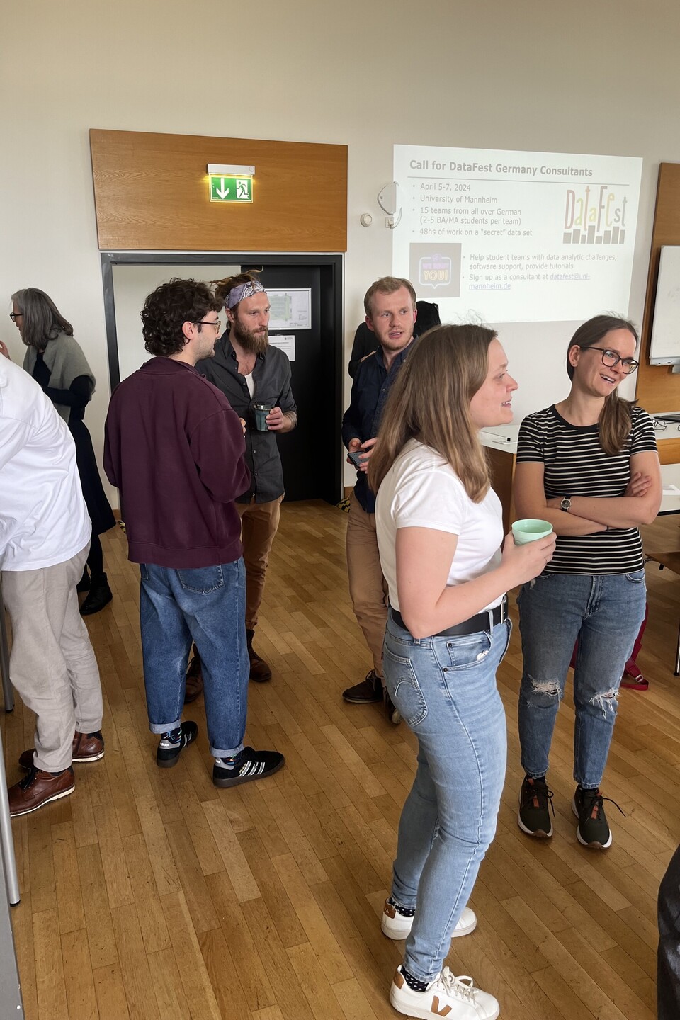 Eine Gruppe von Teilnehmenden unterhält sich in der Pause. Im Hintergrund nehmen sich Personen Kaffee und Snacks.