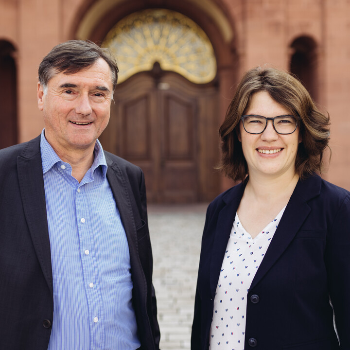 Portraitfoto von zwei Personen. Im Hintergrund das Schloss