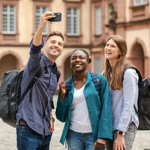 Drei Studierende stehen auf dem Ehrenhof und machen ein Selfie von sich.