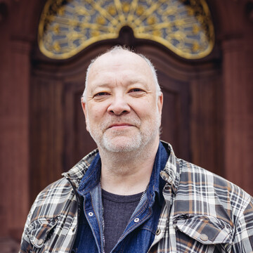 Andreas Wick hat einen grauen Dreitagebart. Er trägt Karo-Hemd über einem Jeans-Hemd.