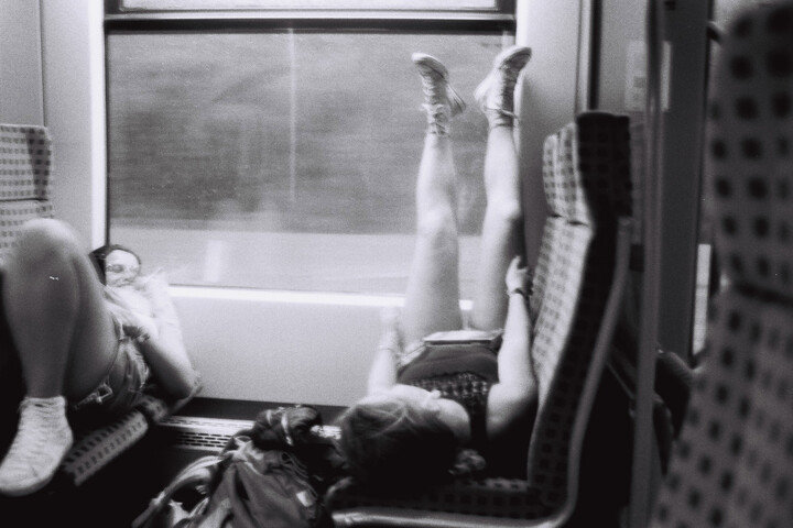 Ein Schwarz-weiß-Foto von zwei Frauen, die auf Sitzen in einer Bahn liegen.