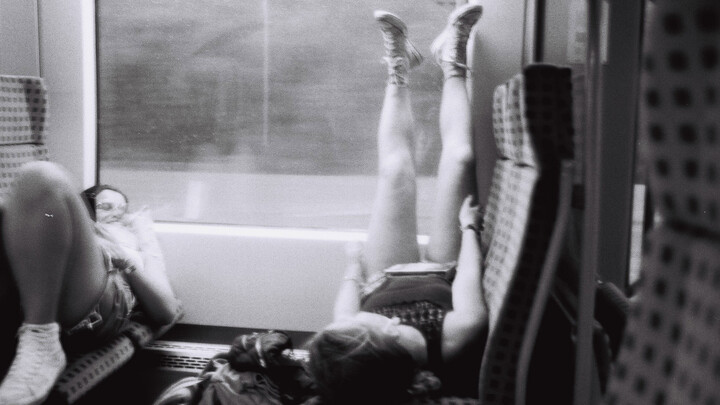 Ein Schwarz-weiß-Foto von zwei Frauen, die auf Sitzen in einer Bahn liegen.