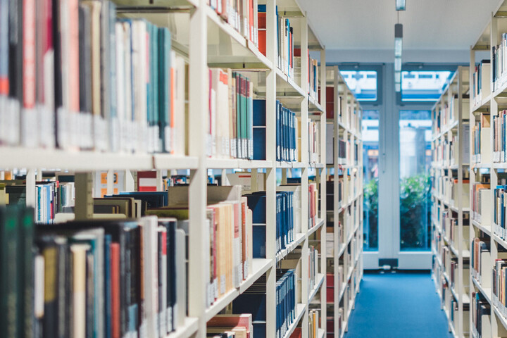 Ein Gang zwischen zwei hohen Bücherregalen voller Bücher in einer Bibliothek