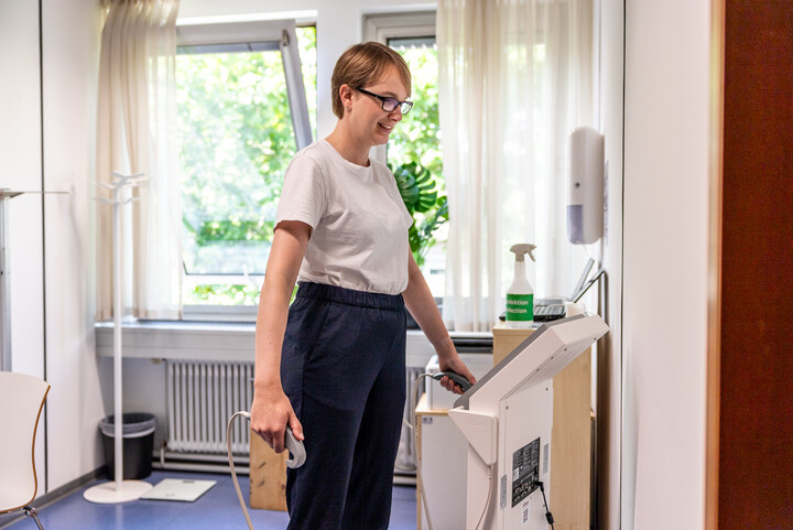 Luisa Gebhardt steht auf einer Waage. Sie hält zwei Messstäbe in der Hand.
