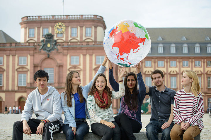 Sechs Studierende sitzen auf einer Bank im Ehrenhof und halten eine Weltkugel hoch.