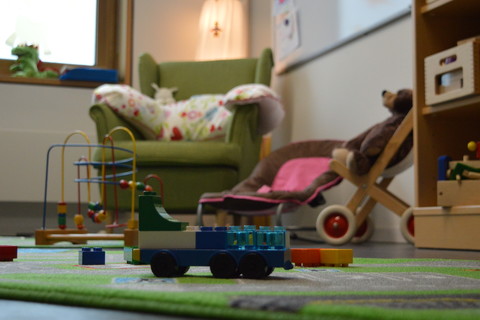 Ein kinderfreundliches Zimmer mit Sessel, bunten Spielsachen und einem Regal.