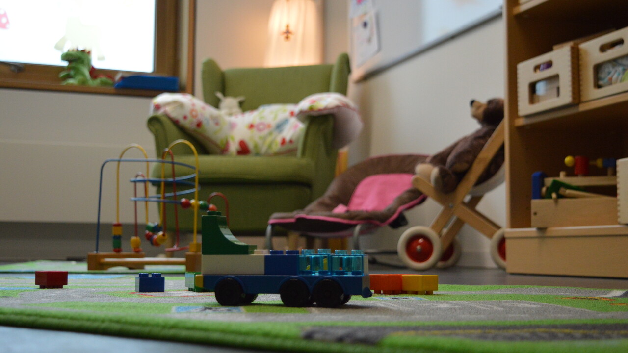 Ein kinderfreundliches Zimmer mit Sessel, bunten Spielsachen und einem Regal.