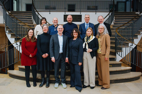 Das Bild ist ein Gruppenfoto vor einer geschwungenen Treppe.
