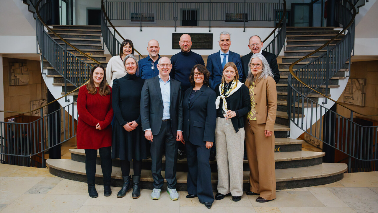 Das Bild ist ein Gruppenfoto vor einer geschwungenen Treppe.