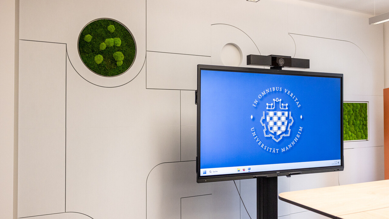 Das Bild zeigt eine schallschluckende Wand mit eingebauten grünen Moos-Elementen. Davor steht ein großes Display mit dem Logo der Uni Mannheim.