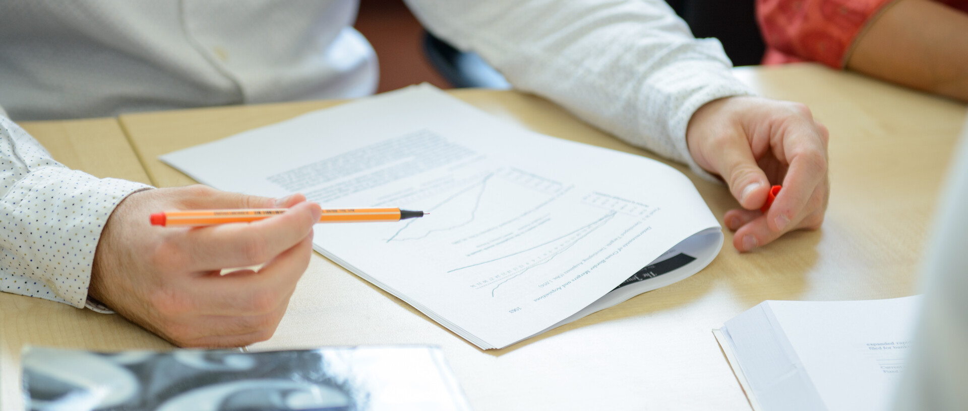 Hände einer Person, die einen Text liest und Stellen mit dem Stift markiert