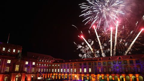 Das Mannheimer Schloss ist in der Dunkelheit blau angestrahlt. Ein Feuerwerk leuchtet am Himmel.