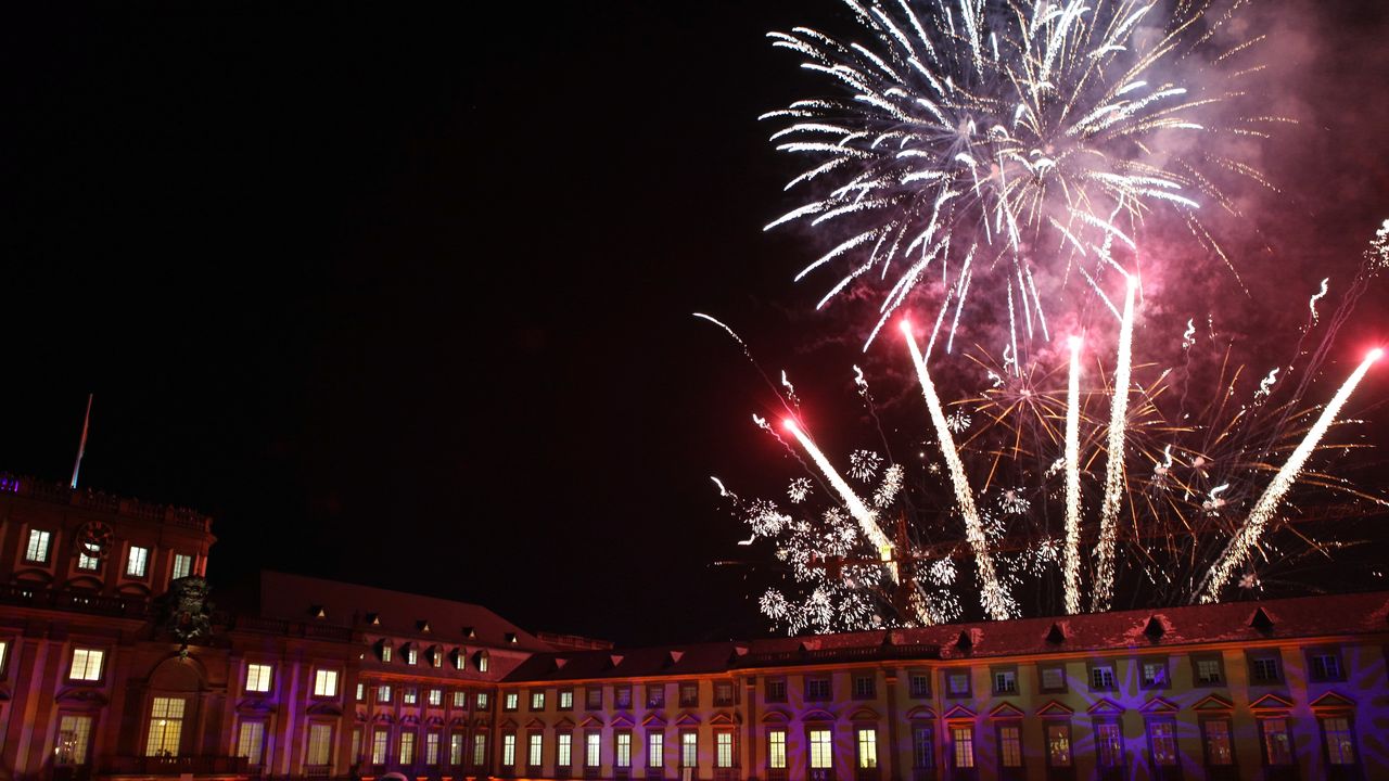 Das Mannheimer Schloss ist in der Dunkelheit blau angestrahlt. Ein Feuerwerk leuchtet am Himmel.