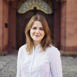 Annkathrin Wiltz lächelt und hat  hellbraunes und schulterlanges Haar. Sie trägt eine weiße Bluse mit goldenen Punken.