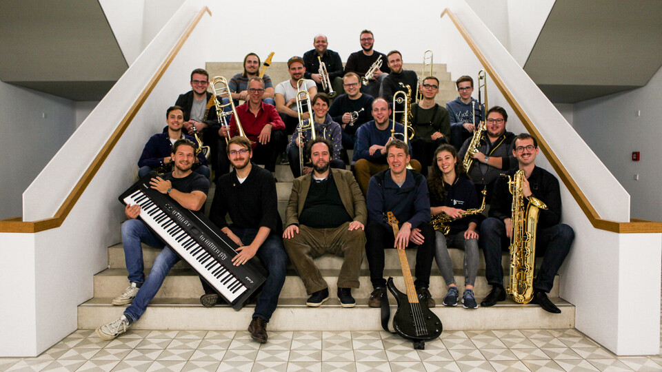 Musikerinnen und Musiker der Bigband sitzen mit Instrumenten auf einer Treppe
