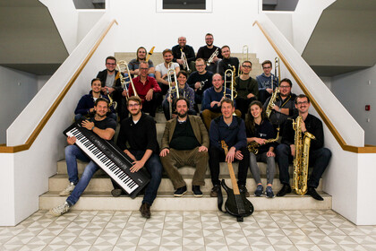 Musikerinnen und Musiker der Bigband sitzen mit Instrumenten auf einer Treppe