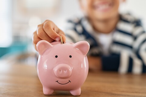Ein Kind steckt eine Münze in ein rosanes Sparschwein.