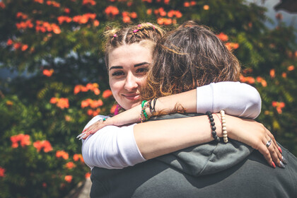 Zwei Personen umarmen sich. Eine Person steht mit dem Rücken zur Kamera, die andere Person lächelt.