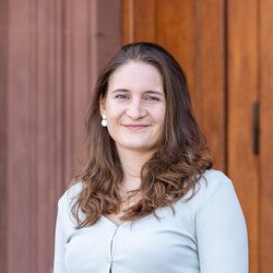 Natalie trägt schulterlanges, dunkelbraunes Haar, einen hellen Pullover und lächelt freundlich in die Kamera