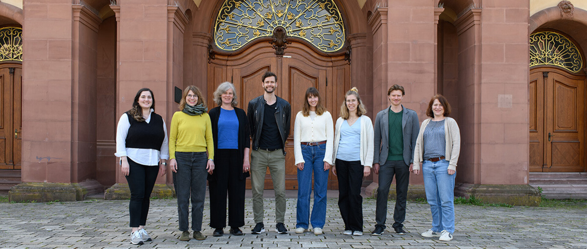Acht Persone stehen nebeneinander vor dem Schloss der Universität.