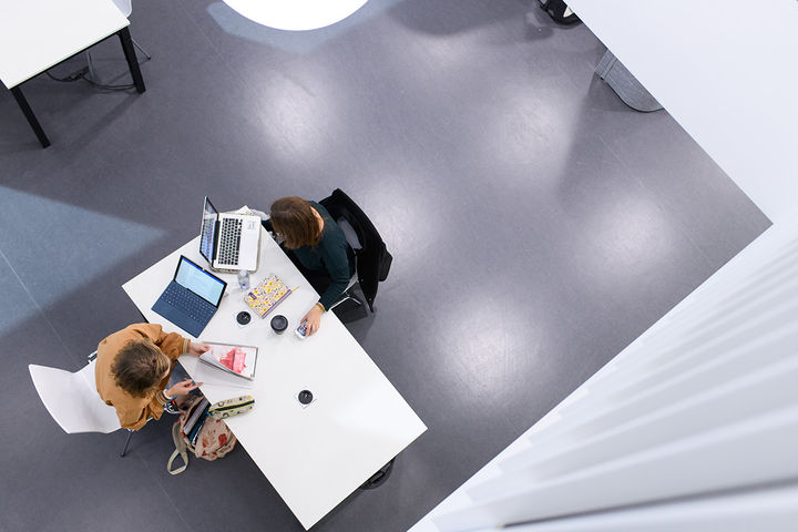 Zwei Personen sitzen an einem Tisch und arbeiten an ihren Laptops. 