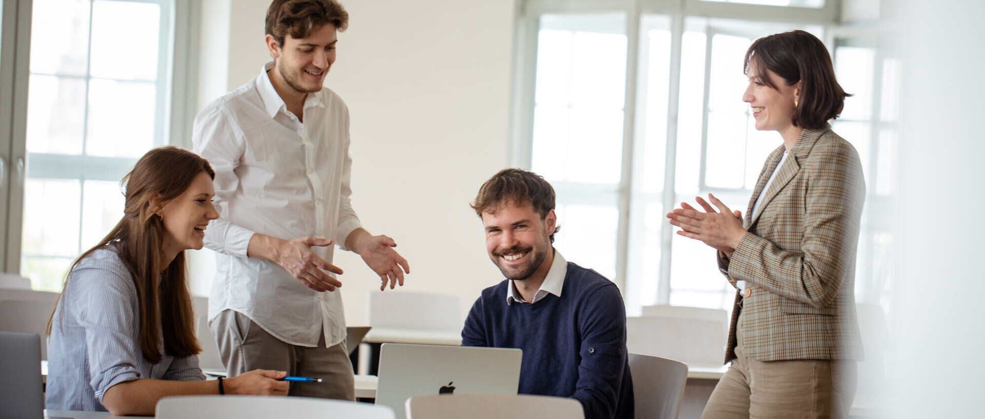 Vier Personen besprechen sich in einem hellen Raum. Zwei von ihnen sitzen, während zwei stehen.