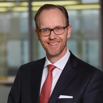 Portrait von Henning Lobin. Er trägt ein weißes Hemd, eine rote Krawatte sowie einen schwarzenn Blazer und lächelt.