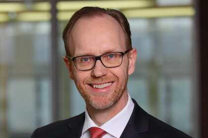 Portrait von Henning Lobin. Er trägt ein weißes Hemd, eine rote Krawatte sowie einen schwarzenn Blazer und lächelt.