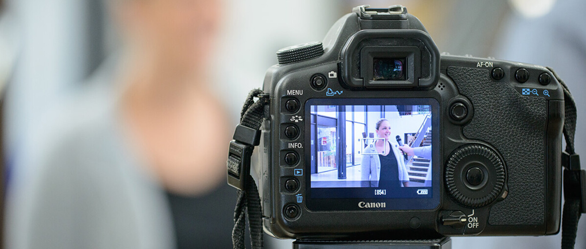 Auf der Bildanzeige einer Digitalkamera ist das Bild einer Frau zu sehen, die mit einem Mikrofon interviewt wird.