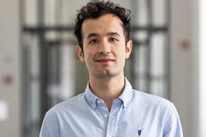 Erken Alapati has short black curly hair. He wears a blue shirt with collar