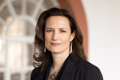 Eine Person trägt eine schwarze Bluse sowie einen schwarzen Blazer und steht vor einem Fenster. Die Person heißt Kirstin Kersten.