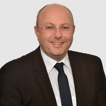 Prof. Stolletz hat eine Brille und trägt einen dunklen Anzug mit Krawatte und weißem Hemd.